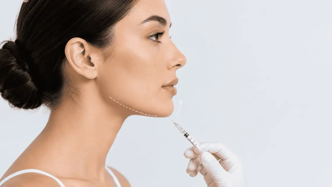 Woman in profile receiving non-surgical chin filler treatment to enhance jawline definition and facial balance.